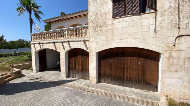 Stone-clad garage with three wooden doors and balcony of the retro villa in Porto Cristo