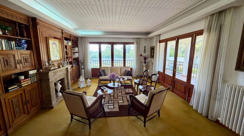 Elegant living room of the retro villa in Porto Cristo with fireplace, wood paneling and balcony access.