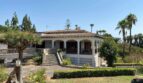 Outside view of a Mediterranean villa in Porto Cristo with columned veranda, staircase, terracotta roof and palms.