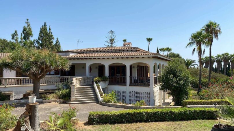 Outside view of a Mediterranean villa in Porto Cristo with columned veranda, staircase, terracotta roof and palms.