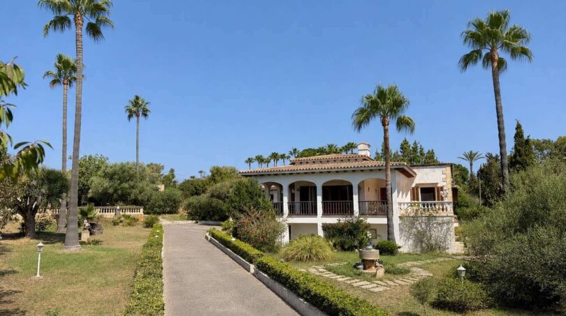Outside view of a Mediterranean villa in Porto Cristo with well-maintained garden, palms and covered terrace.