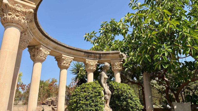 Semi-circular columned colonnade with sculpture and trees in the garden of the retro villa in Porto Cristo.
