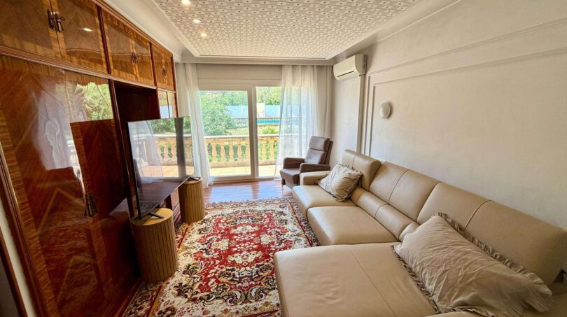 Living room of the retro villa in Porto Cristo with leather sofa, wooden cabinet and balcony access.