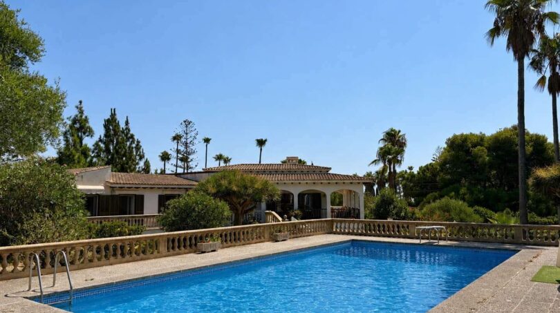 Large outdoor pool of the retro villa in Porto Cristo with Mediterranean balustrade and palm garden