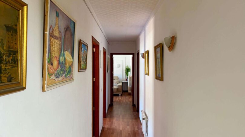 Long hallway of the retro villa in Porto Cristo with parquet floor, red doors and paintings on the walls.