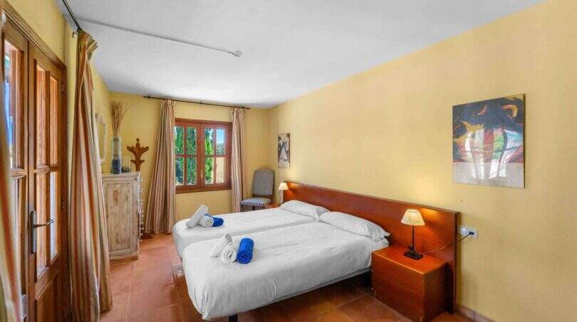 Helles Schlafzimmer der Windmühlen-Finca in Felanitx mit Doppelbett, Terrakottaboden und gelben Wänden.