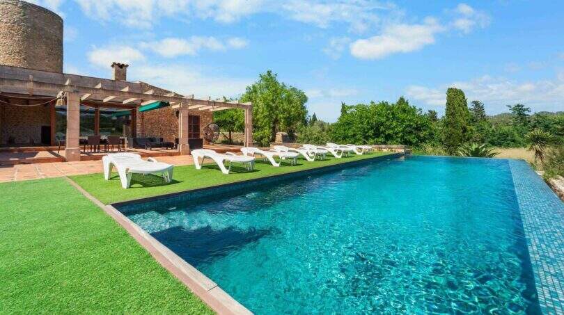 Großer Infinity-Pool mit weißen Liegestühlen, Pergola und Steinhaus der Windmühlen-Finca in Felanitx