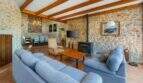 Rustikales Wohnzimmer der Windmühle Felanitx mit Steinwänden, Holzbalken, blauen Sofas und Kaminofen.