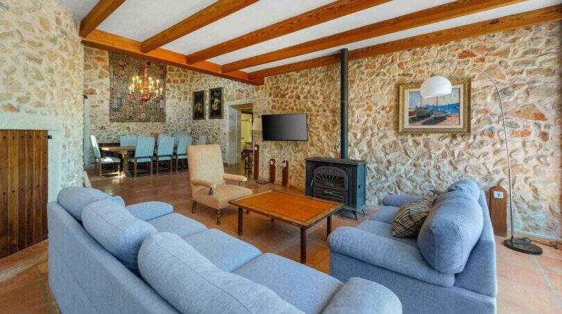 Rustikales Wohnzimmer der Windmühle Felanitx mit Steinwänden, Holzbalken, blauen Sofas und Kaminofen.