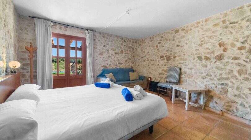 Rustikales Schlafzimmer der Windmühle in Felanitx mit Natursteinwänden, Doppelbett und Terrakottaboden.