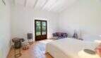 Bright bedroom of the Felanitx finca with terracotta floor, wooden beam ceiling and terrace door to the garden.