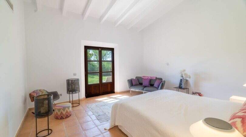 Bright bedroom of the Felanitx finca with terracotta floor, wooden beam ceiling and terrace door to the garden.