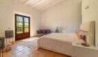 Bright bedroom of the Felanitx finca with terracotta floor, wooden beam ceiling and French doors to the garden.