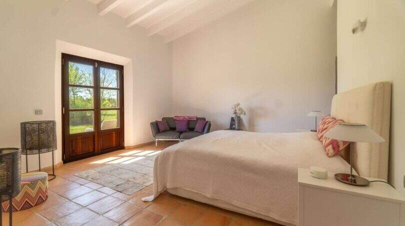 Bright bedroom of the Felanitx finca with terracotta floor, wooden beam ceiling and French doors to the garden.