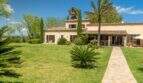 Exterior view of the Felanitx finca with well-maintained lawn, palm trees, stone path and Mediterranean facade with terracotta roof.
