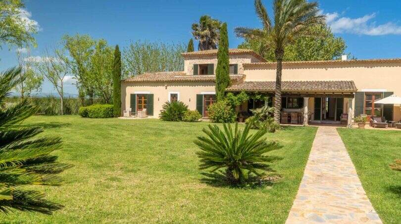 Exterior view of the Felanitx finca with well-maintained lawn, palm trees, stone path and Mediterranean facade with terracotta roof.