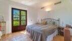 Bright bedroom of the Felanitx finca with double bed, terracotta floor and wooden door to the garden.