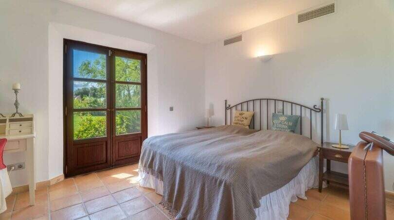 Bright bedroom of the Felanitx finca with double bed, terracotta floor and wooden door to the garden.