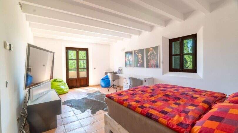 Spacious bedroom of the Felanitx finca with wooden beam ceiling, double bed and basketball wall decoration.