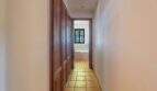 Narrow hallway with wooden cabinets and terracotta floor, leading to a bathroom with window, Felanitx finca