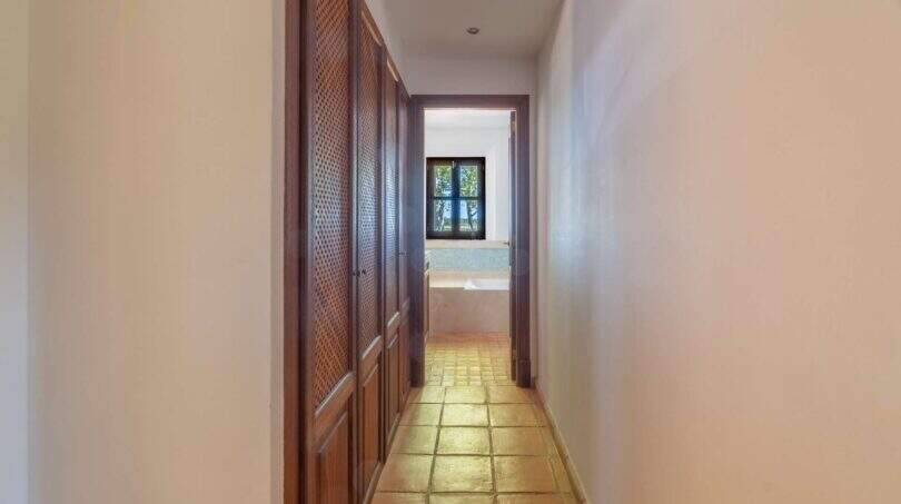 Narrow hallway with wooden cabinets and terracotta floor, leading to a bathroom with window, Felanitx finca
