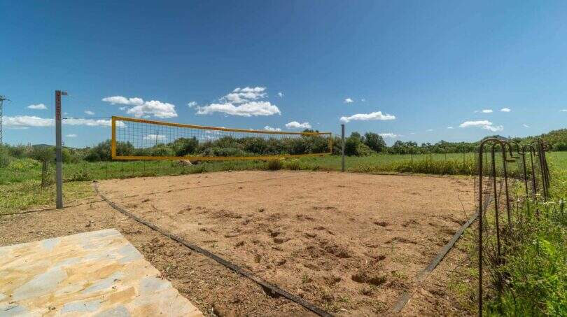Sand volleyball court with yellow net on exclusive finca in Felanitx, surrounded by green landscape.