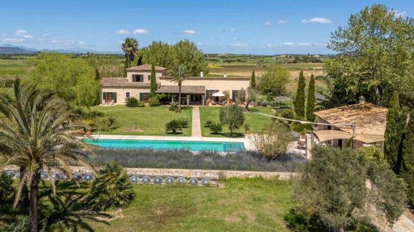 Aerial view of an exclusive finca in Felanitx with pool, garden facilities, palm trees and vineyards in the background.