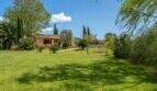 Spacious garden of the Felanitx finca with well-maintained lawn, palm trees, cypress trees and Mediterranean outdoor facilities.