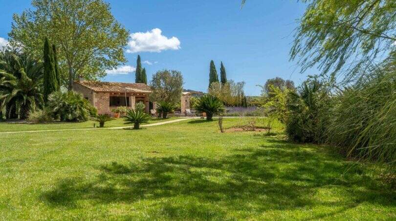 Spacious garden of the Felanitx finca with well-maintained lawn, palm trees, cypress trees and Mediterranean outdoor facilities.
