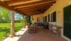 Covered terrace of the Felanitx finca with wooden beams, stone pillars, dining table and barbecue station