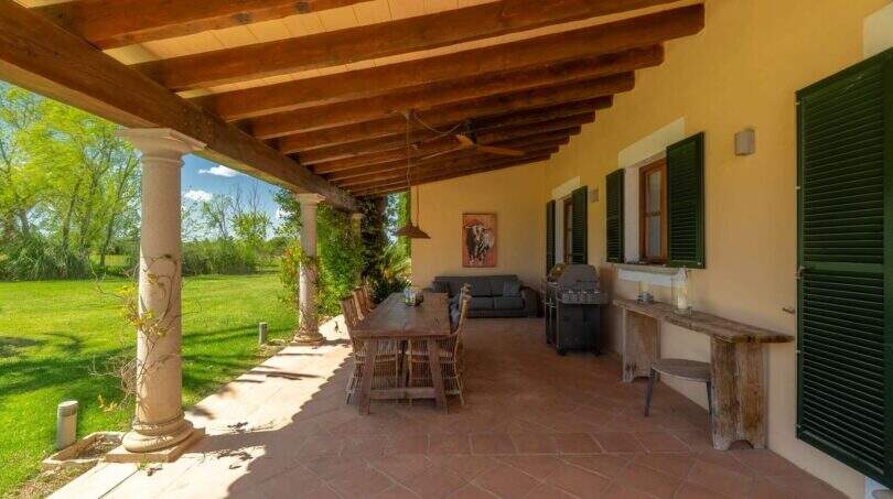 Covered terrace of the Felanitx finca with wooden beams, stone pillars, dining table and barbecue station