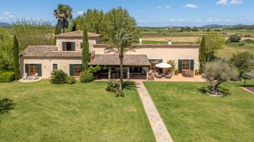 Aerial view of the exclusive Felanitx finca with natural stone path, palm trees, green shutters and expansive landscape.