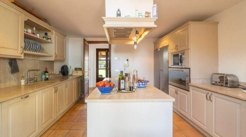 Bright country kitchen with kitchen island, built-in appliances and terracotta floor in exclusive Felanitx finca