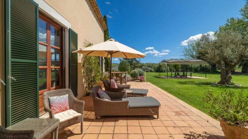 Sunny terrace of the Felanitx finca with rattan furniture, sun umbrella and well-maintained garden with olive tree