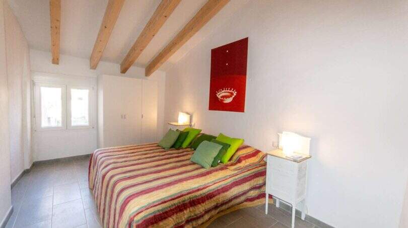 Schlafzimmer mit Doppelbett, bunter Tagesdecke, Holzbalkendecke und rotem Kunstwerk in Stadthaus Felanitx