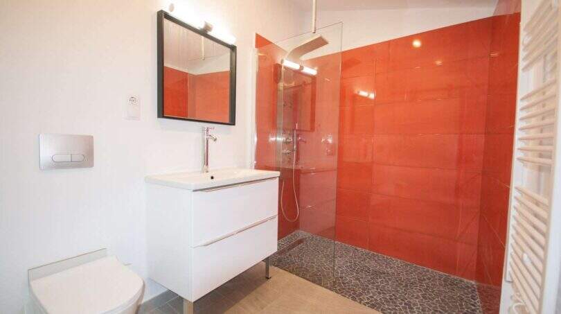 Modernes Badezimmer mit roter Duschfliese, Glastrennwand, Wandtoilette und weißem Waschtisch im Stadthaus Felanitx