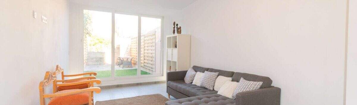 Helles Wohnzimmer mit grauem Ecksofa, Terrassenzugang zum Garten und modernen Fliesen im Stadthaus Felanitx.