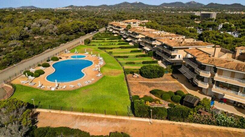 Luftaufnahme Wohnanlage Porto Colom mit großem Pool, gepflegten Grünanlagen und mediterranen Terrassenhäusern umgeben von Pinienwald.