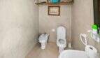 Helles Badezimmer der Wohnung in Porto Colom mit WC, Bidet, Holzregal und beigefarbenen Fliesen.