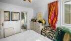 Helles Schlafzimmer der Wohnung in Porto Colom mit weißem Bett, bunten Vorhängen und Kommode
