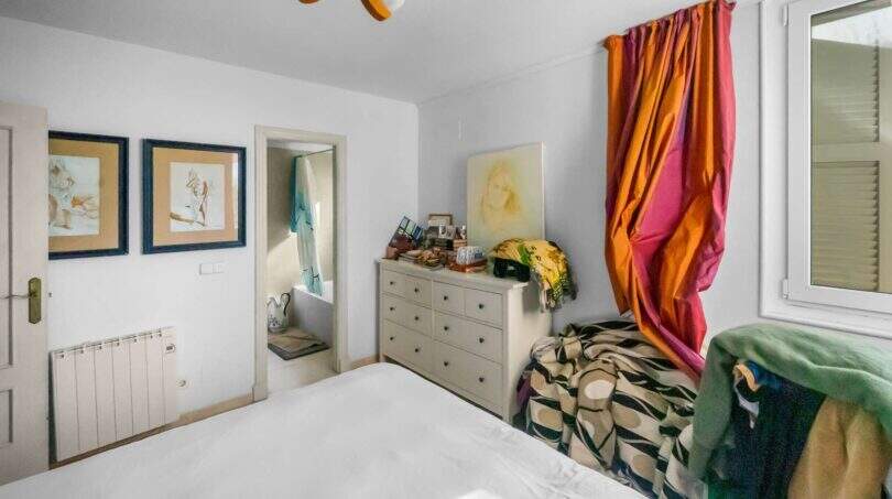 Helles Schlafzimmer der Wohnung in Porto Colom mit weißem Bett, bunten Vorhängen und Kommode