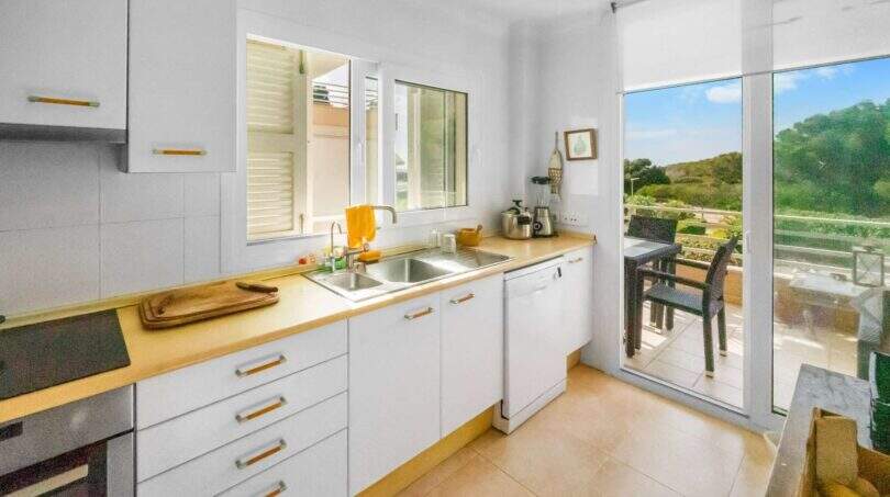 Helle Küche mit weißen Schränken, Holzarbeitsplatte und Glasschiebetür zur Terrasse mit Meerblick in Porto Colom