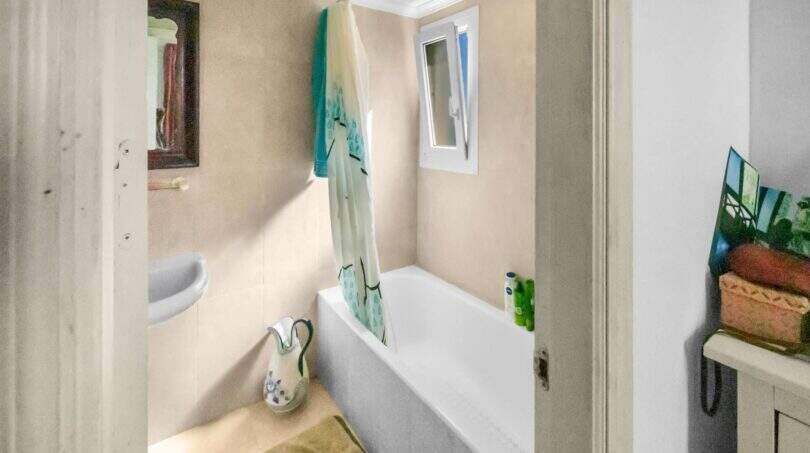 Helles Badezimmer der Wohnung in Porto Colom mit Badewanne, Duschvorhang, Spiegel und kleinem Fenster.