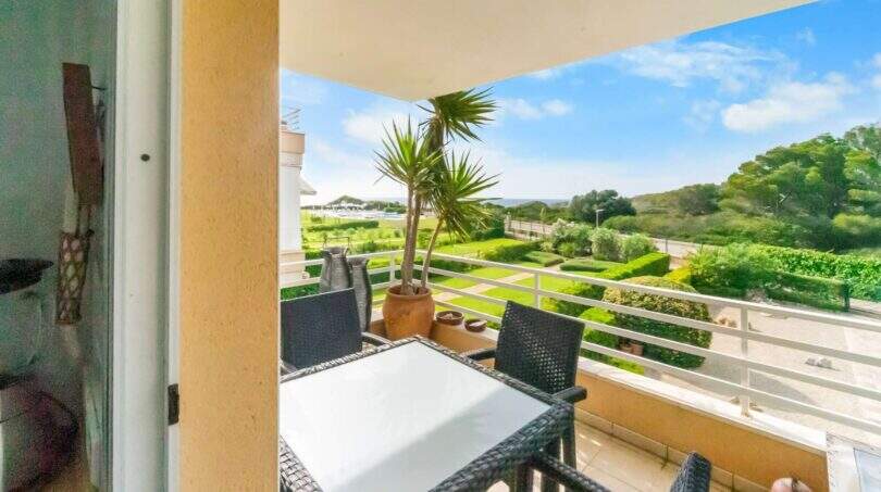 Sonnige Terrasse mit Rattanmöbeln und Palme, Blick auf grüne Gartenanlage und Meer in Porto Colom