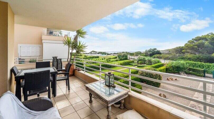 Geräumige Terrasse der Wohnung in Porto Colom mit Rattanmöbeln, Gartenblick und Meerblick im Hintergrund.