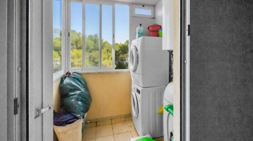 Utility-Raum der Wohnung in Portocolom mit Waschmaschine, Trockner und Fenster mit Blick ins Grüne.
