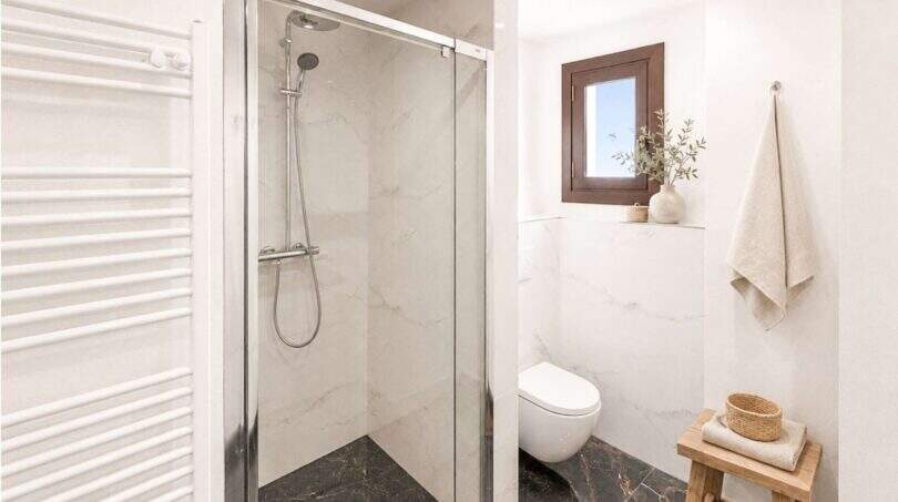 Modernes Badezimmer mit Glasdusche, Marmorfliesen, Handtuchheizung und rustikalem Holzhocker in Felanitx
