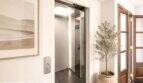 Moderner Aufzug mit Edelstahlinnenraum, Olivenbaum und Holztür in eleganter Wohnung in Felanitx