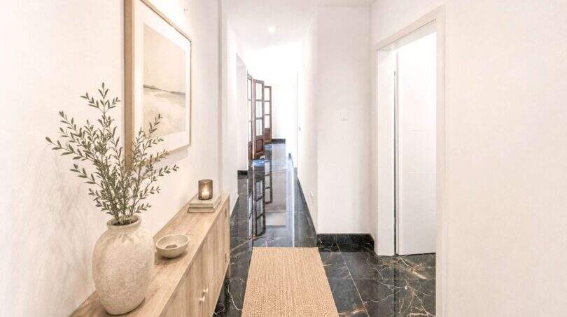 Eleganter Flur der Wohnung in Felanitx mit dunklem Marmorboden, Holzkommode und modernem Naturdekor.