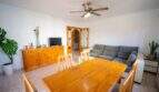 Helles Wohn-Esszimmer mit Holztisch, grauem Sofa, Deckenventilator und Bogendurchgang in Einfamilienhaus Porto Colom